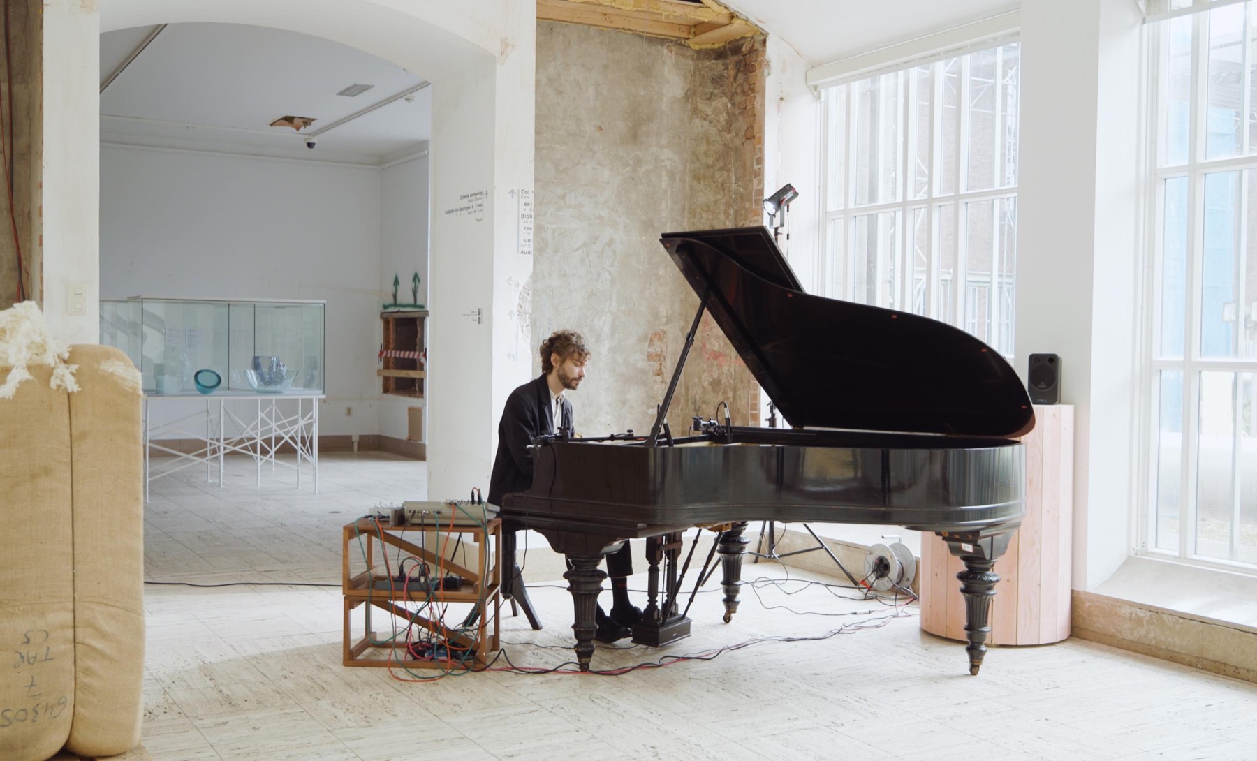 Playing a grand piano in an empty museum gallery with a stripped brick wall